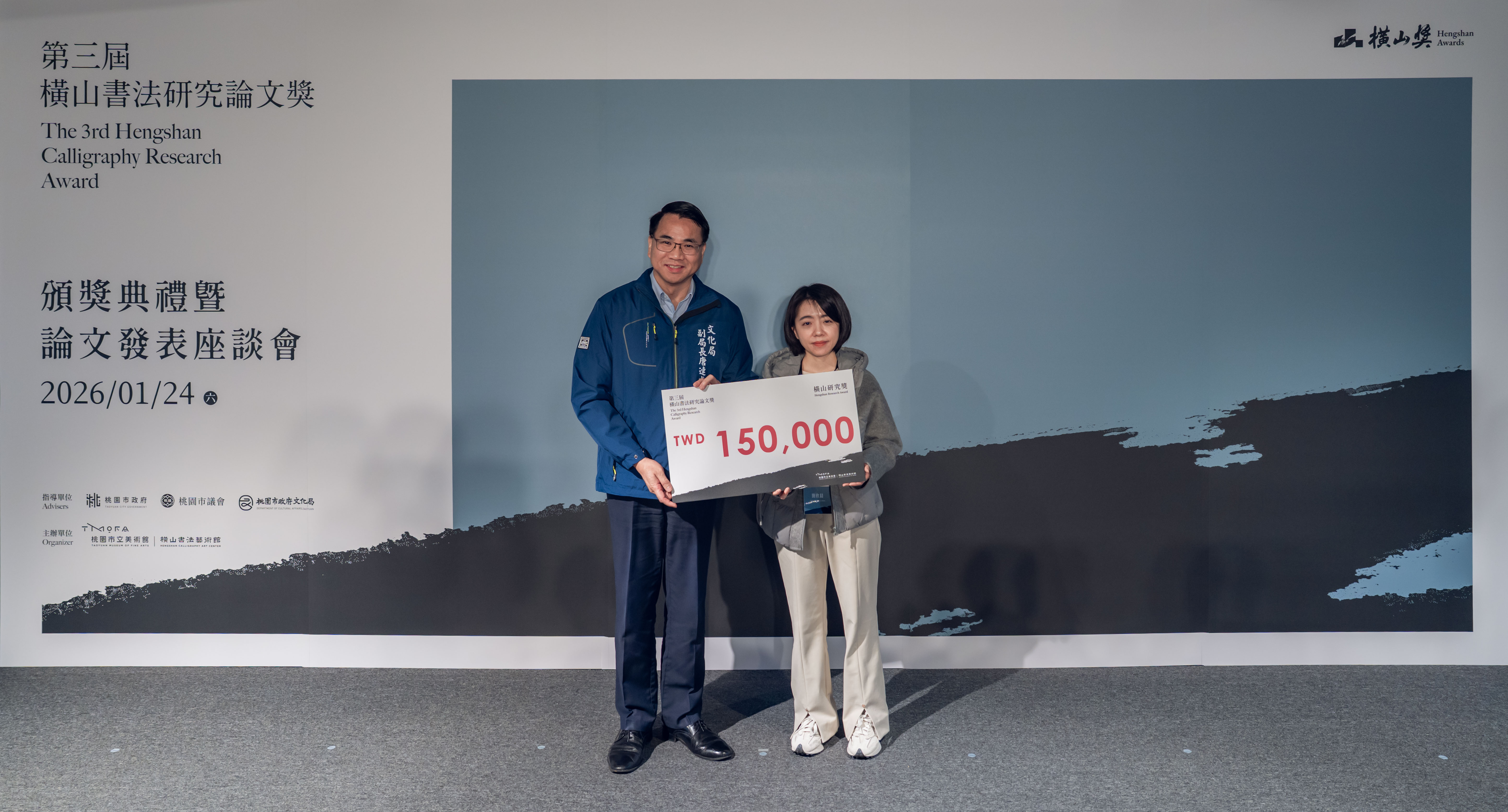 桃園市政府文化局副局長唐連成(左)頒發首獎「橫山研究獎」，由簡欣晨(右)獲得，獲獎論文為「康熙皇帝的集字活動──從幾件董其昌（款）古詩十九首談起」，獎金新臺幣15萬元。攝影／眼福映像—周廷瑋